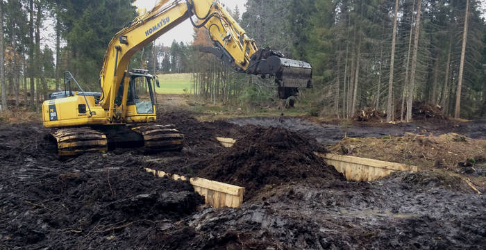 Les palissades en bois sont recouvertes de tourbe afin d’éviter leur pourrissement à long-terme. Elles deviennent ainsi invisibles à nos yeux. La rétro-pelleteuse utilisée est spécialement équipée afin de respecter le sol sensible de la tourbière.